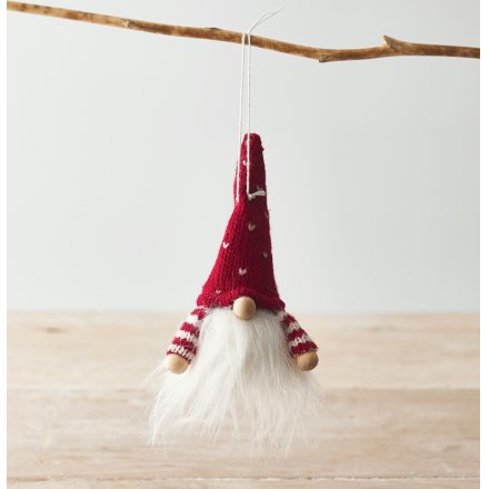 Decorative gnome with a red hat and white beard hanging from a branch on a light wooden surface.