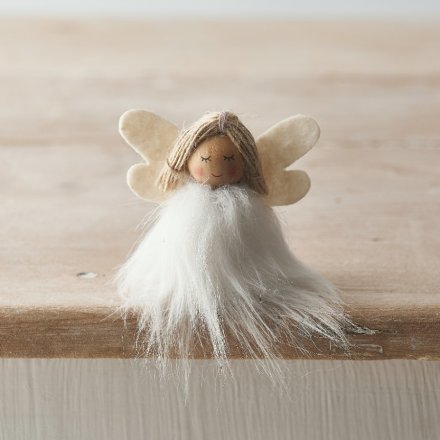 Small angel figurine with white hair and beige wings on a wooden surface