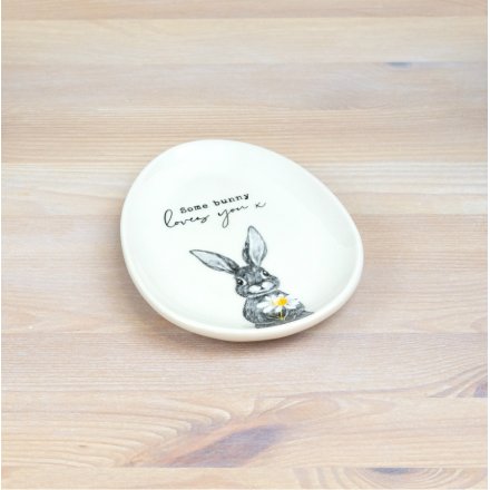 Whote ceramic egg shaped plate with cute bunnny sketch at the bottom holding a daisy. Above has the quote 'some bunny loves you'