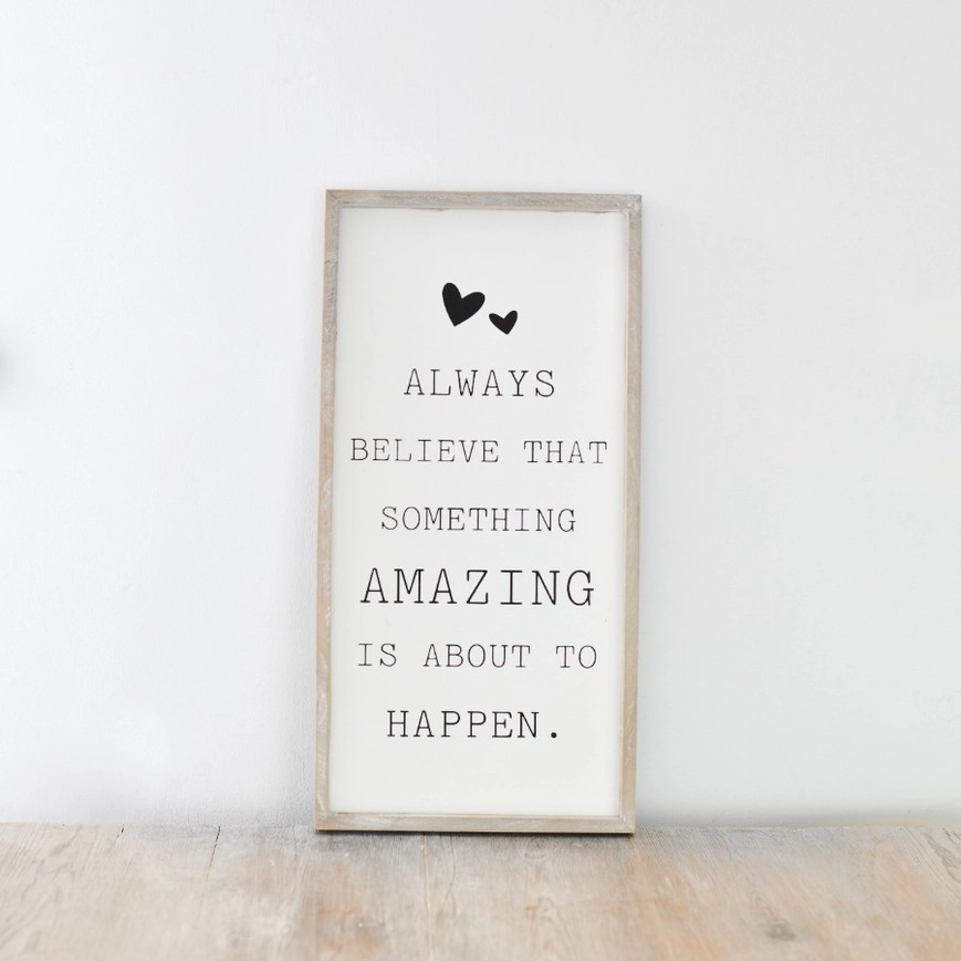 Wooden framed sign featuring the phrase  'always believe that something amazing is about to happen' in a typewriter style font. 
