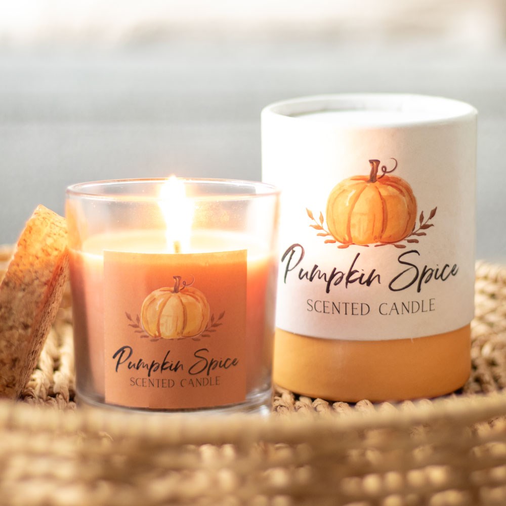 Pumpkin spice scented candle and matching cardboard tube packaging on a woven surface with a blurred background