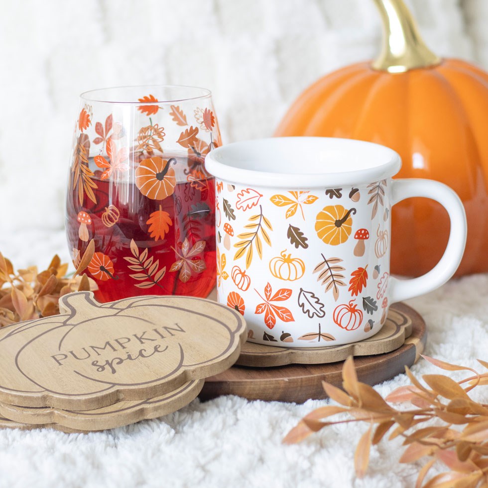Mug with autumn-themed design, glass with pumpkin spice label, and pumpkin on a white background
