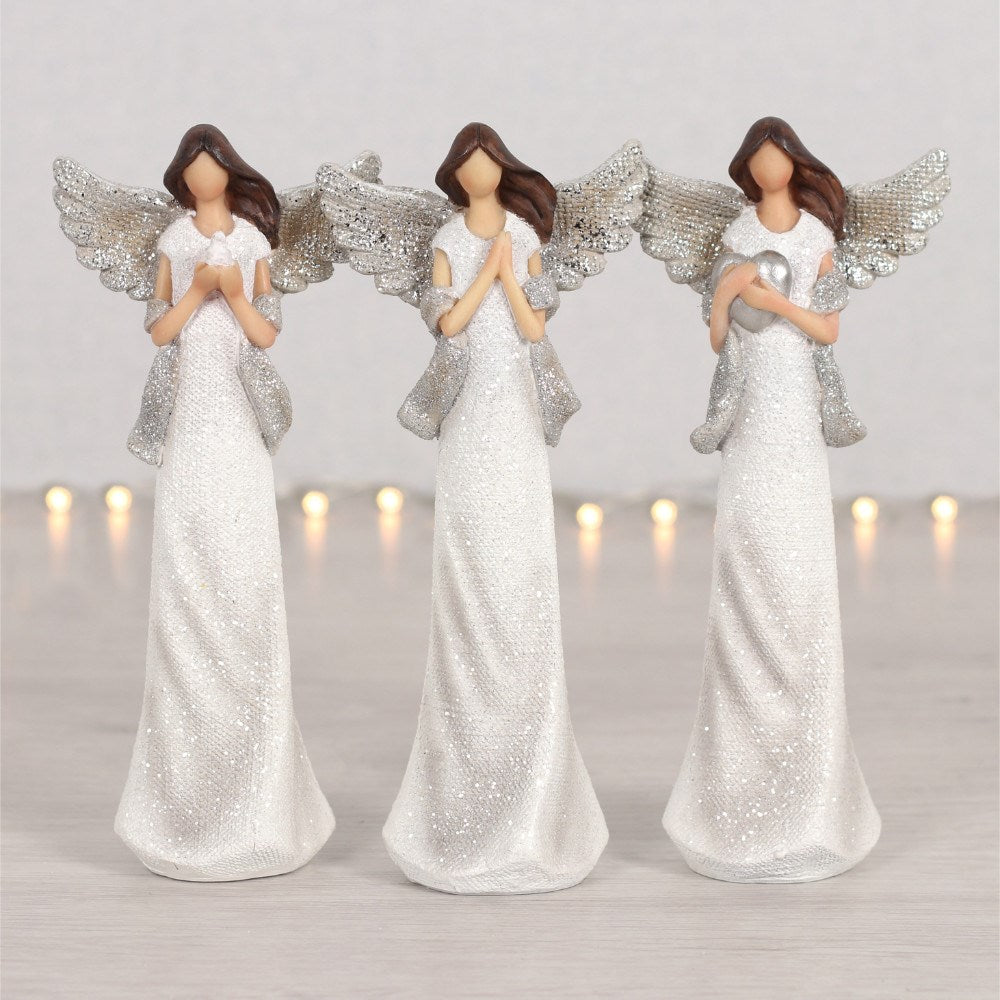 Three angel figurines with white dresses and silver wings on a light background