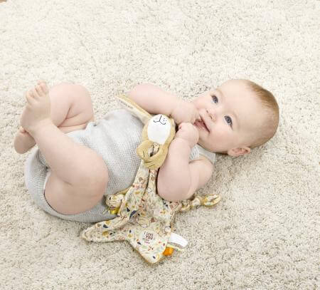 Baby lying on a carpeted floor with the baby comforter.