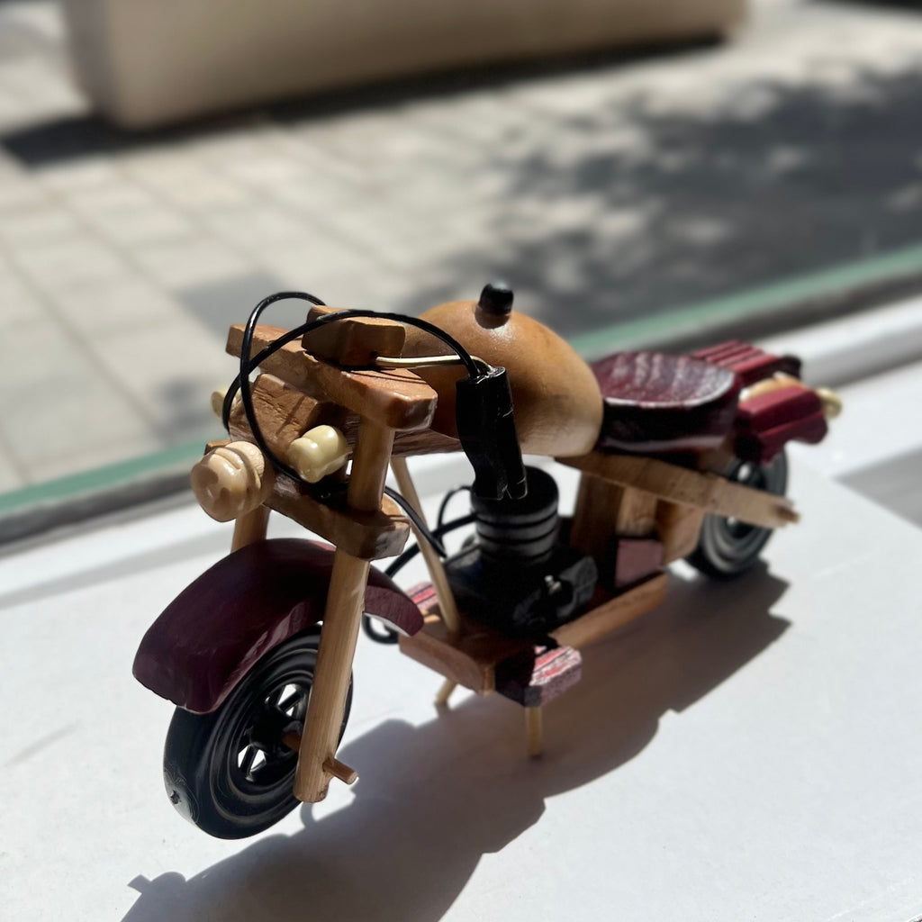 Wooden vintage style motorcycle on its stand. Features natural, red, and black stained wood. 