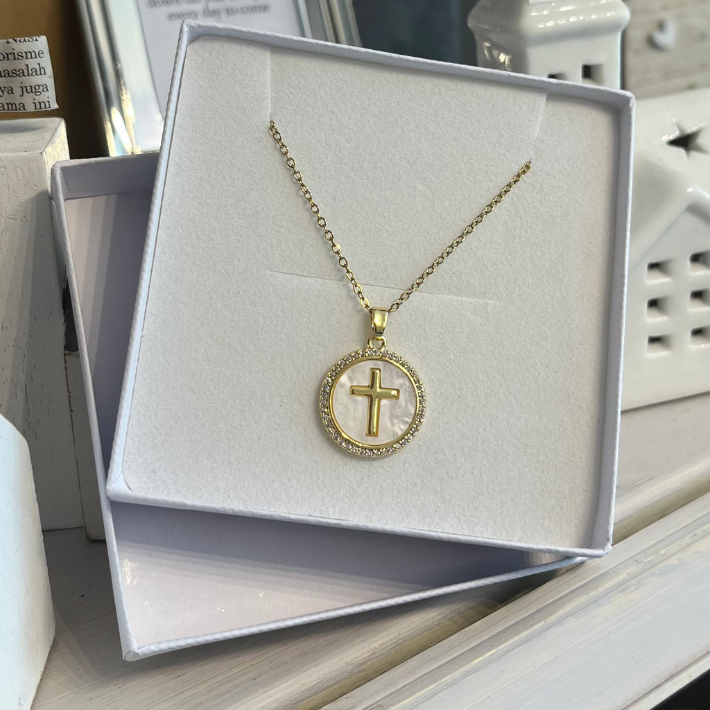 Gold chain necklace with a circle pendant. features crystals around the circumference of the pendant, a pearlescent background inside the pendant and a gold cross in the middle.