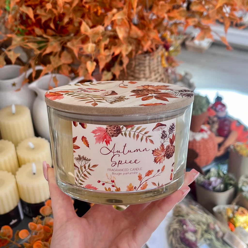 Autumn Spice scented candle with autumnal-floral packaging on a blurred background. 