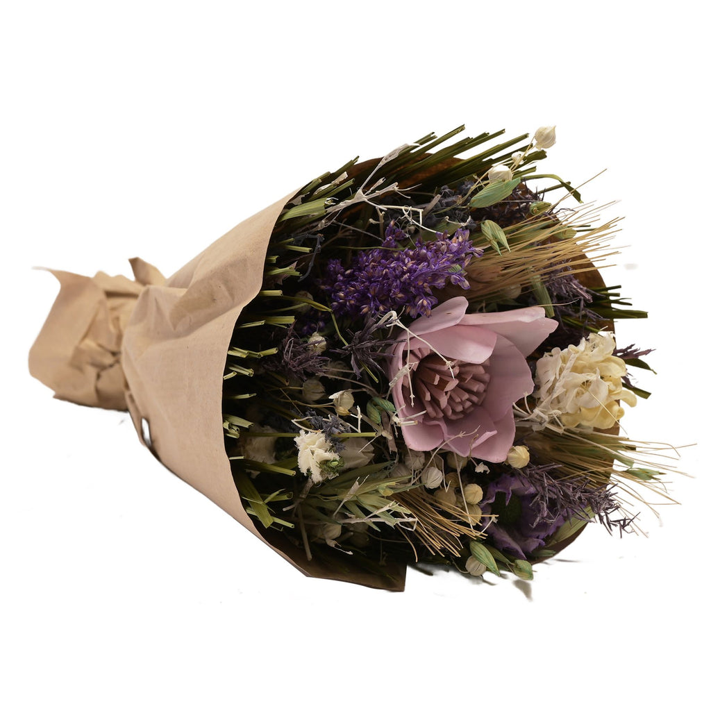 Faux floral bouquet wrapped in brown paper featuring misc leaves and flowers in purple, white, and green with one big lilac flower.