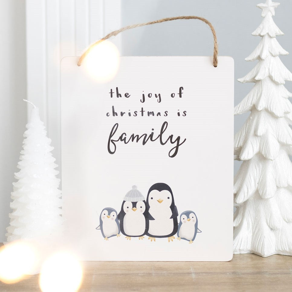 Decorative sign with family of penguins and 'the joy of Christmas is family' text, hanging against a light background.