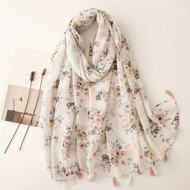 Cream scarf featuring beige flowers. Tassels on the edge of the scarf alternate pink and white. 