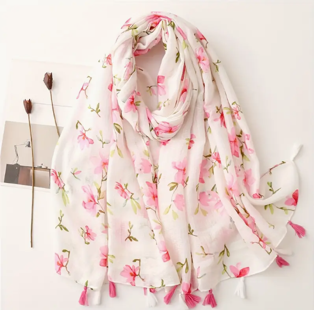 White scarf with pink flower design, and alternating pink and white tassels on the scarf edge. 