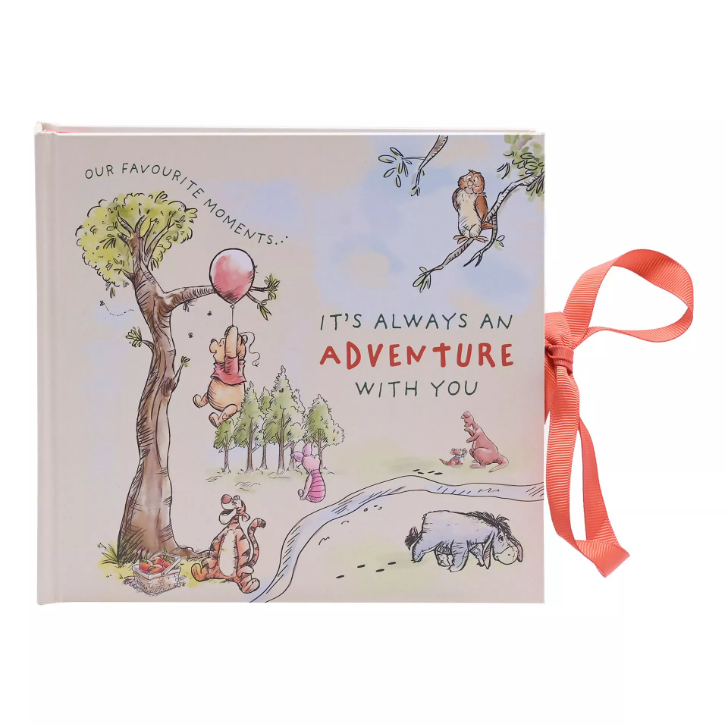 Photo albun front. Features red ribbon fastener. Front design is Winnie the Pooh floating past a tree on the left holding onto a red balloon with Tigger watching from below. Piglet is sat with his back facing us behind a stream. Kanga and Roo are further down the stream and on the right. Owl is on a branch in the top right corner. Eeyore is on the close side of the stream on the right with footsteps trailing behind him. The quote 'Our favourite moments... it's always an adventure with you' is in the spaces.