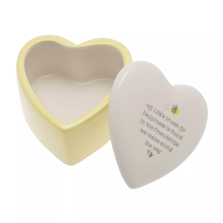 Heart shaped trinket box with white lid and yellow body. On lid features the quote 'Life's truest happiness is found in the friendships we make along the way' with a little bee above the quote and two little hearts below the quote.