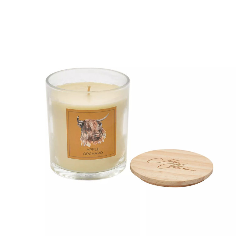 White candle in clear glass jar with watercolour highland cow image on an orange square label on the front. Features wooden lid with 'meg hawkins' signature engraved on top.