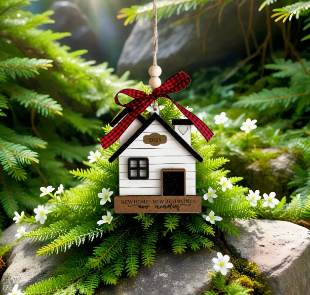 black and white house handing ornament. Features a plaid red and black bow attached to the hanging feature. House sits on brown wooden rectangle with the text 'new home, new beginnings, new memories
