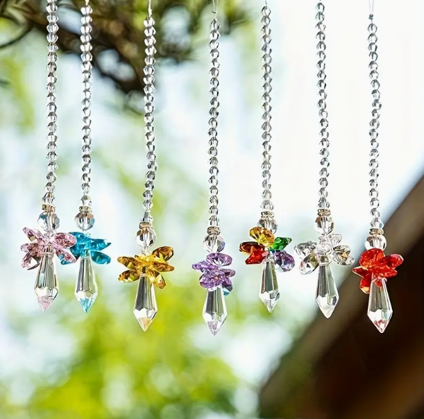 Colorful crystal hanging decorations with simplistic angel designs against a blurred natural background