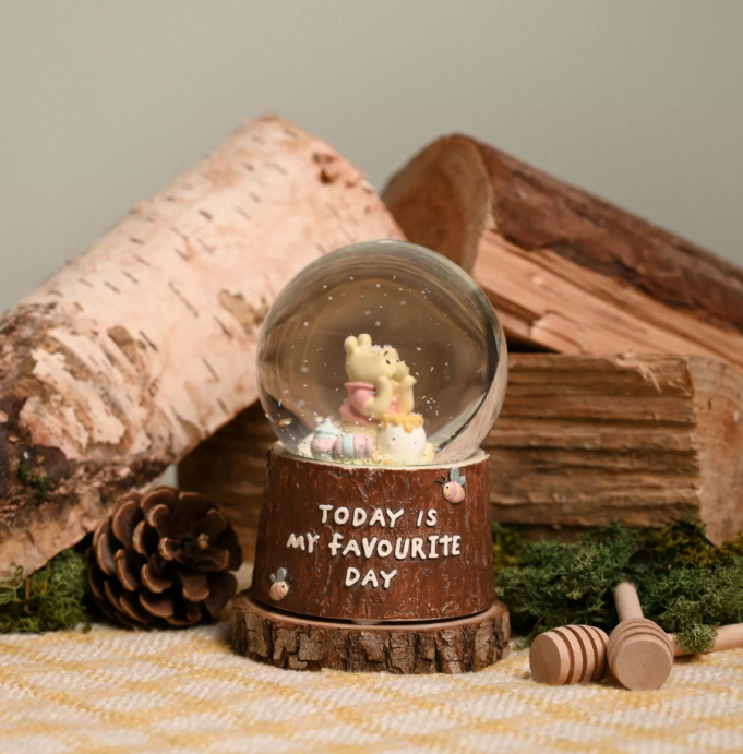 Snowlglobe on wooden tree trunk style base with the quote 'today is my favourite day' in handwritten font. Inside the snowglobe is Winnie the Pooh resting his chin on his hands on a pot of hunny with a couple of smaller empty honey pots beside him. 