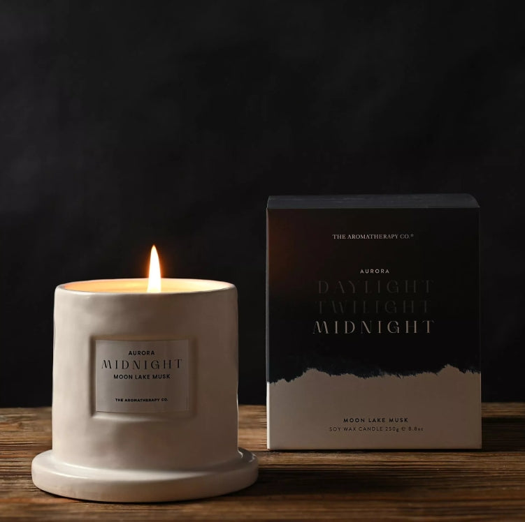 Candle and packaging of The Aromatherapy Co. Aurora Midnight candle on a wooden surface with a dark background.