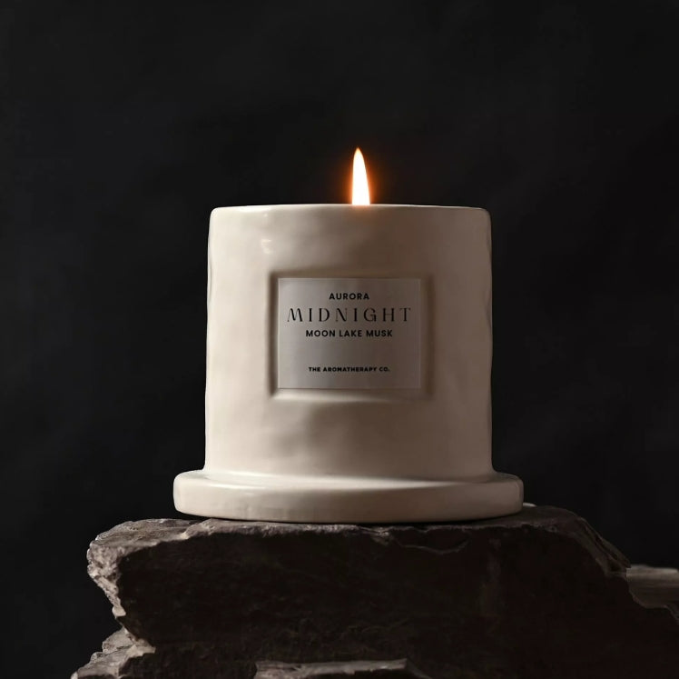 White candle labeled 'Aurora Midnight Moon Lake Musk' on a dark background
