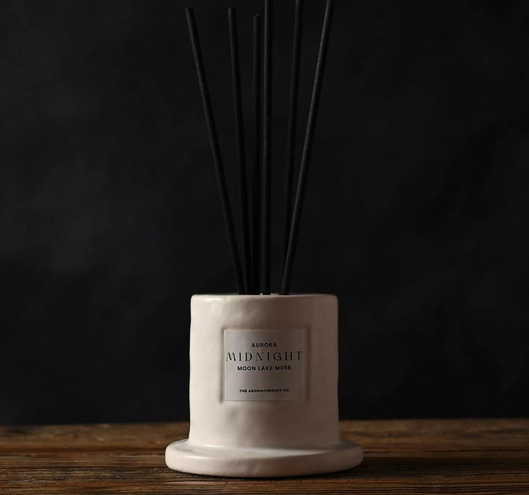 White diffuser with black reeds on a wooden surface against a dark background