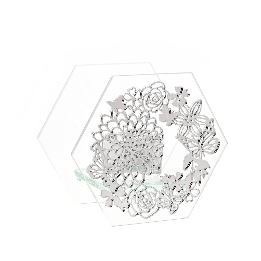 Glass tealight holder sitting int between two hexagon pieces of glass, the front piece covered in silver butterfly design with flowers. 