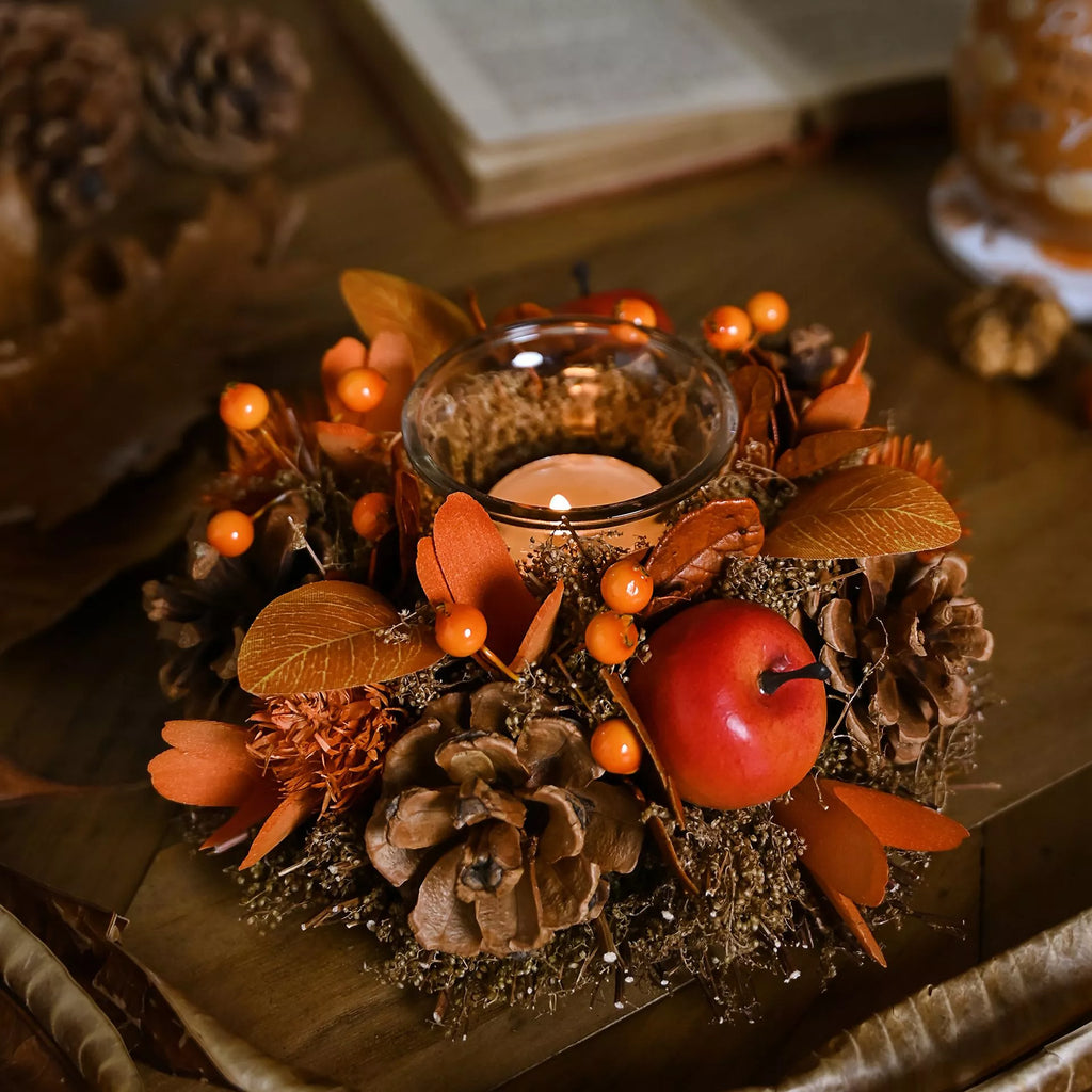Decorative fall arrangement with candles, apples, and pinecones on a wooden surface.
